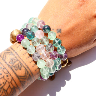 An assortment of semi transparent beads. Purple, blue, clear & green beads with a few brass accent beads and a brass Often Wander charm.