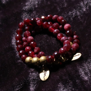 Beautiful faceted round ruby colored jade beads strung together on a beaded bracelet with brass accents and an often wander charm.