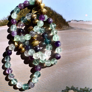 An assortment of semi transparent beads. Purple, blue, clear & green beads with a few brass accent beads and a brass Often Wander charm.