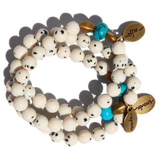 white beads with black specks with one blue accent bead and accent brass beads, along with an Often Wander charm.