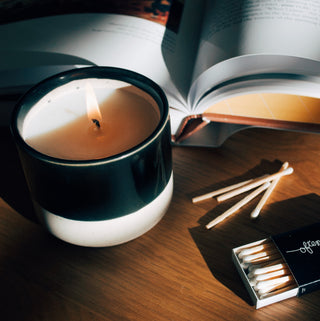 a small lit candle on a table with some matches and an open book