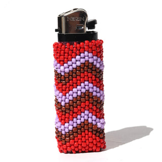 A classic NEON lighter covered in a handmade beaded sleeve featuring a geometric zigzag pattern of red, brown, and light purple beads, set against a plain white background.