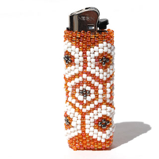 A beaded cylindrical lighter cover with a geometric pattern of orange, white, and black seed beads, shown on a white background with a cast shadow.