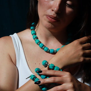 A woman wearing a turquoise beaded necklace and matching bracelet, with dramatic side lighting against a dark background.