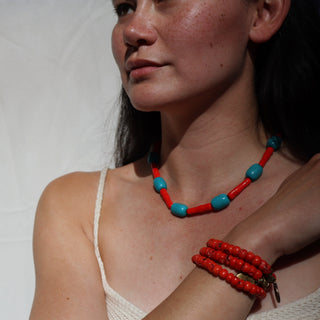 Woman wearing a red and blue beaded necklace and bracelet against a white background