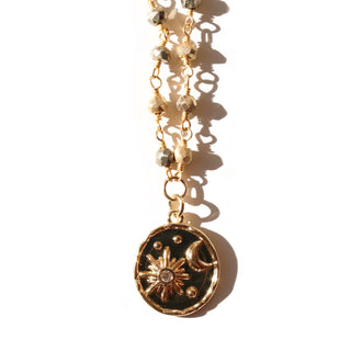 A shiny gold pendant with a crystal studded crescent moon with sun rays hanging from a pyrite beaded rosary chain