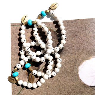 white beads with black specks with one blue accent bead and accent brass beads, along with an Often Wander charm.