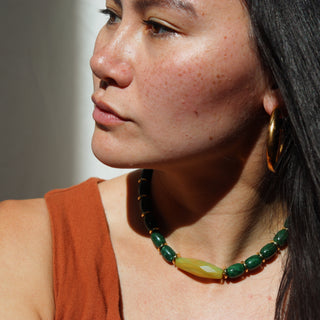 Woman wearing a green beaded necklace and gold hoop earrings against a neutral background