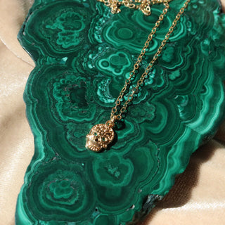Golden skull necklace on dainty gold chain. The eyes of the skull have emerald colored diamond eyes.