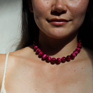 Close-up of a person wearing a pink beaded necklace against a neutral background