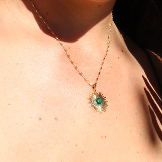 A shiny gold necklace in the shape of a sunburst pendant with a malachite accent in the middle