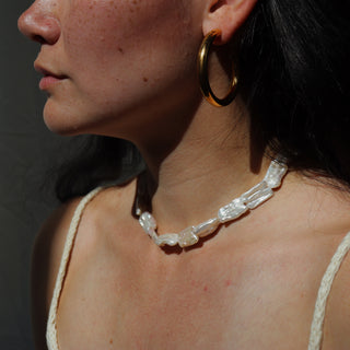 Close-up of a person wearing a pearl necklace and gold hoop earrings against a neutral background