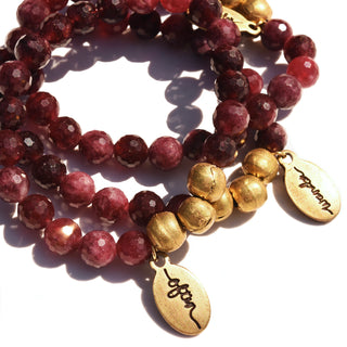 Beautiful faceted round ruby colored jade beads strung together on a beaded bracelet with brass accents and an often wander charm.