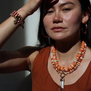 Woman wearing an orange necklace and bracelets, with a neutral background
