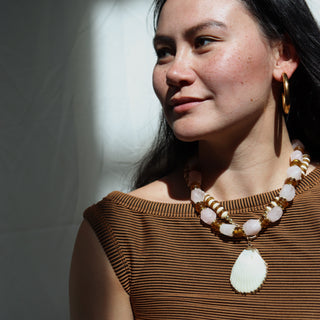 Woman wearing a brown top and gold necklace with large earrings against a neutral background