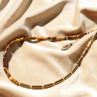 Asymmetrical design with Tiger's Eye tube beads on one side, shiny gold tube beads on the other side and a Often Wander charm  on the back of the necklace