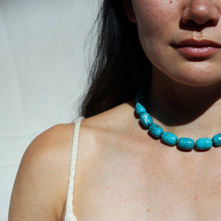 Person wearing a turquoise necklace against a white background