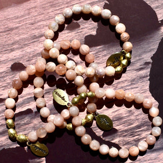 Faceted peachy moonstone beads with brass accent beads, along with an Often Wander charm.