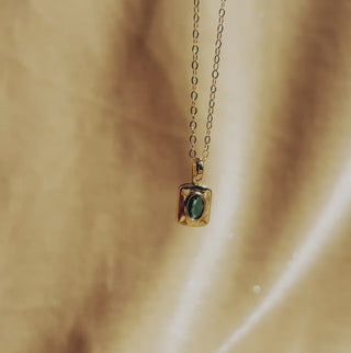 A rounded square 16k gold filled brass pendant with an oval emerald colored faceted stone on dainty 14k gold fill chain.
