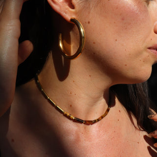 Asymmetrical design with Tiger's Eye tube beads on one side, shiny gold tube beads on the other side and a Often Wander charm on the back of the necklace