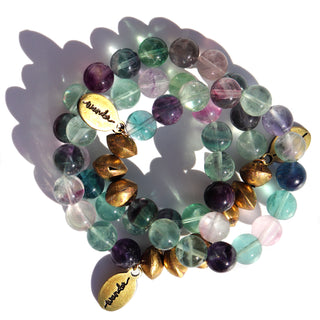 An assortment of  semi transparent beads. Purple, blue, clear & green beads with a  few brass accent beads and a brass Often Wander charm.