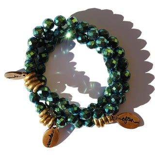 Faceted shiny metallic green hued beads strung together on a beaded bracelet with 3 brass accent beads with a small Often Wander Charm.